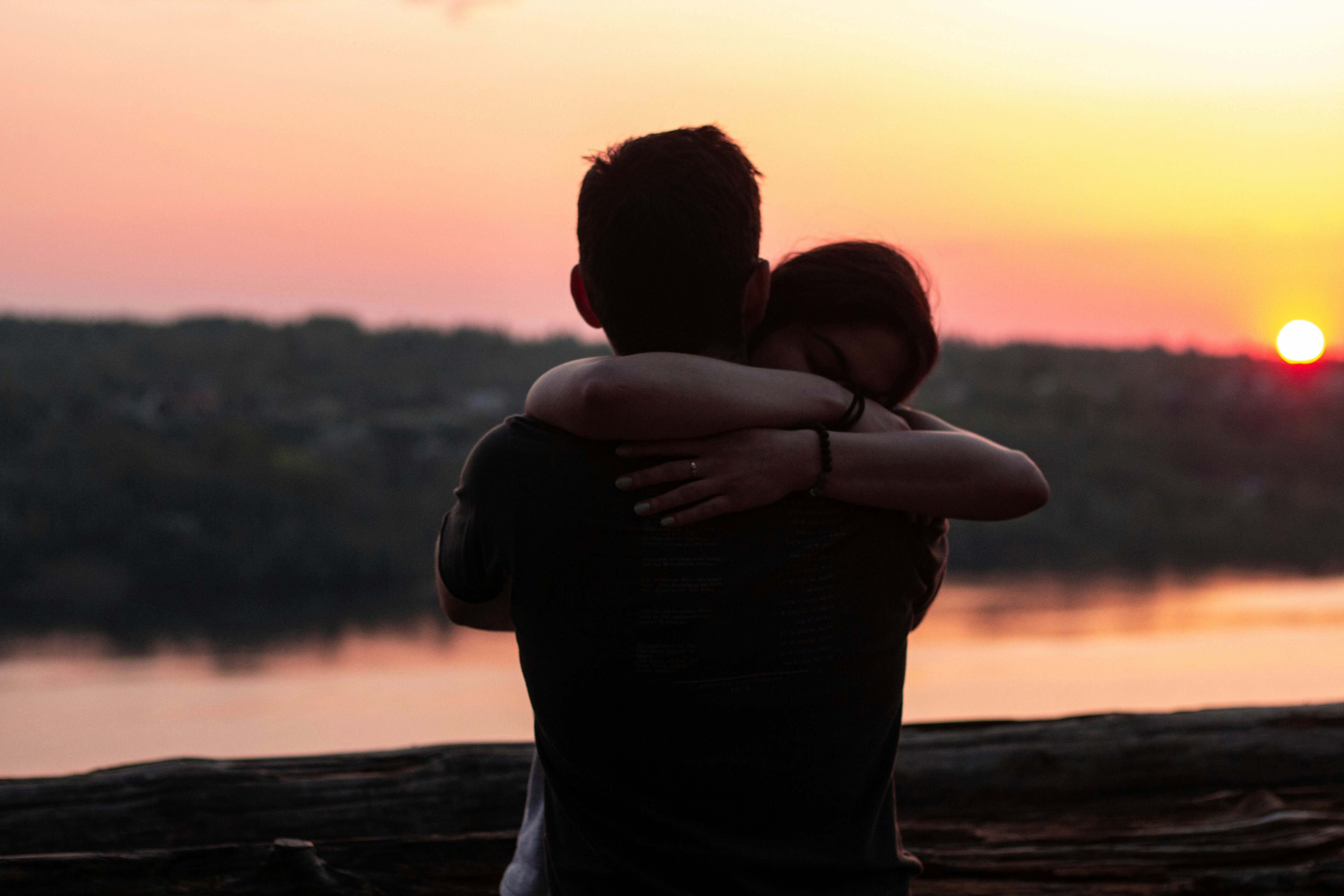 Casal jovem abraçado em cena romântica sob luz quente do pôr do sol