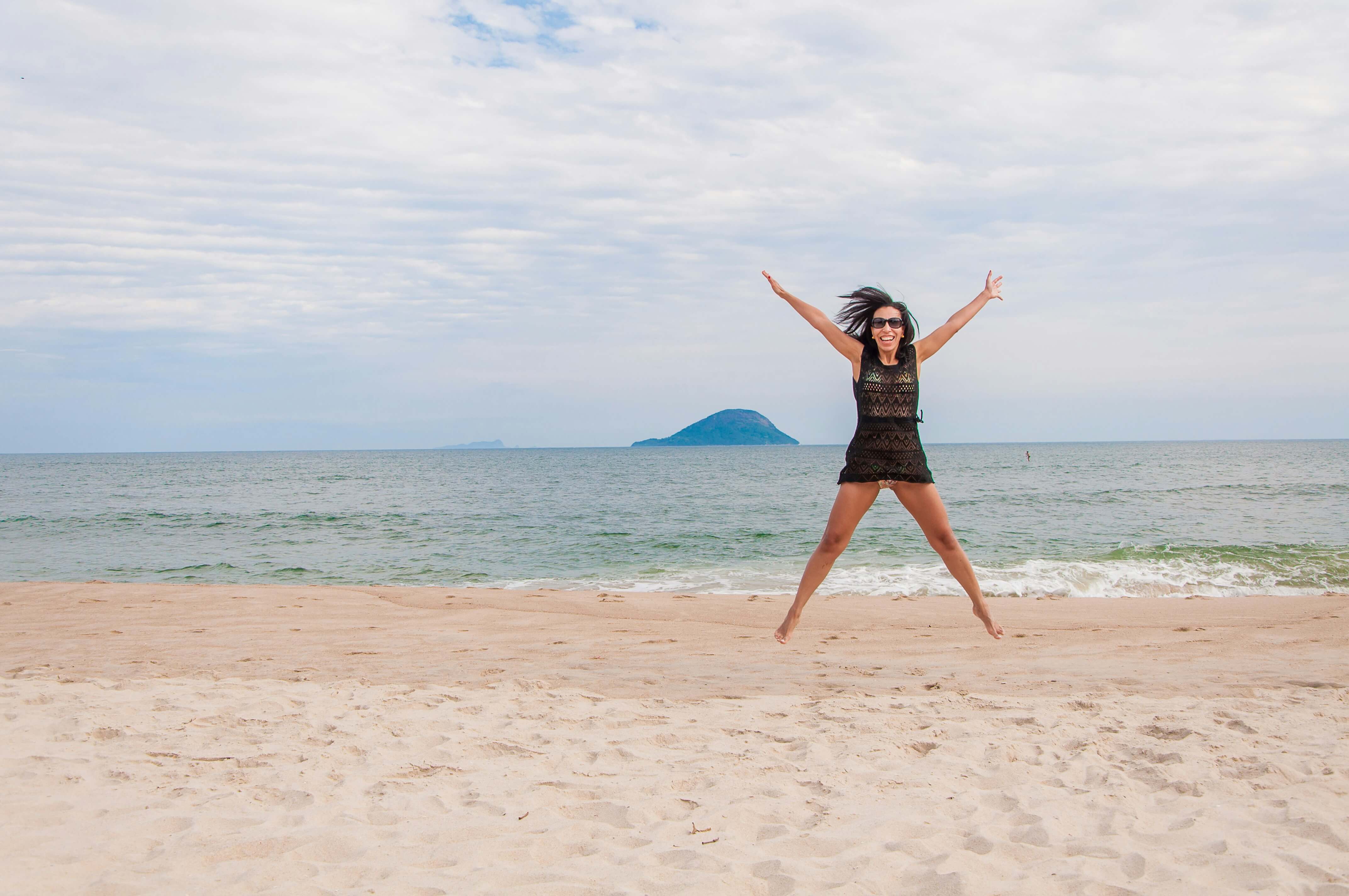Mulher de braços abertos saltando em frente ao mar durante viagem